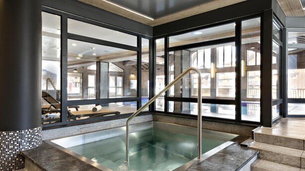 Une piscine intérieure moderne avec des parois en verre transparent, une rampe en métal et un bord carrelé.
