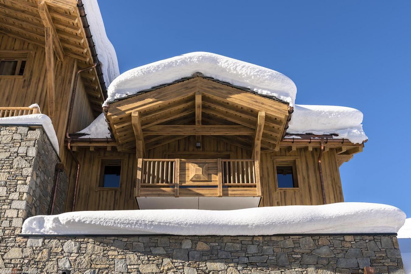 Eine Holzhütte mit Steinfundament, schneebedecktem Dach und einem Balkon mit Geländer.