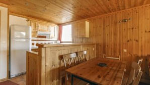 Een houten interieur met een keukenhoek, een eettafel en stoelen.