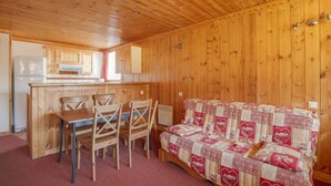 Een gezellig chaletinterieur met een houten eettafel en stoelen, een gewatteerde bank en een kitchenette met houten kastjes.