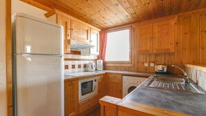 Een compacte keuken met houten kastjes, een koelkast, een magnetron, een wasmachine en een spoelbak.