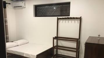Un dormitorio con cama, un armario de madera, una ventana con diseño de celosía y un equipo de aire acondicionado.