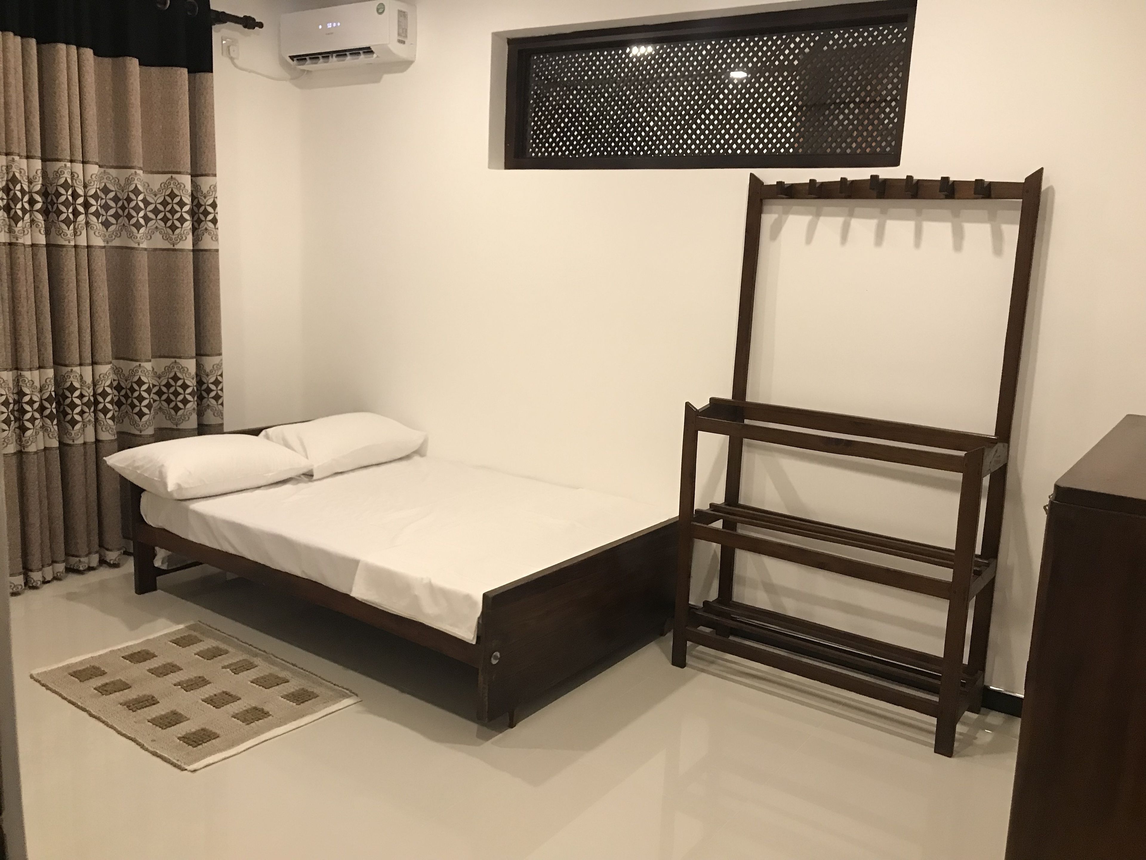 Un dormitorio con una cama, un armario de madera, una ventana con diseño de celosía y un aire acondicionado instalado en la pared.