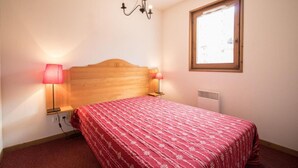 A bedroom with a wooden headboard, a red patterned bedspread, two bedside lamps, and a window with blinds. - 10m from ski slopes, 1st floor, balcony, tv, ski locker, 40m², Val Cenis (Lanslevillard)