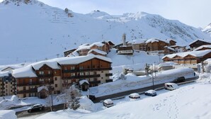 Un centro turístico nevado en la montaña con edificios de madera, un telesilla y una carretera con coches estacionados.