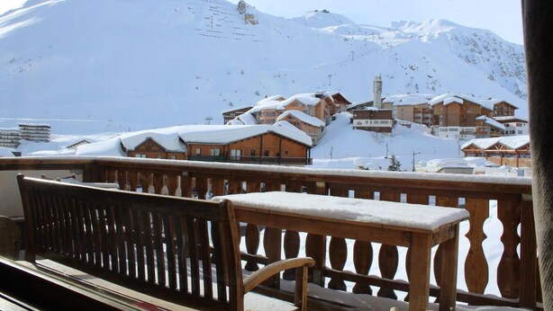 Una montaña nevada con un telesilla al fondo y edificios de madera con nieve en los tejados.