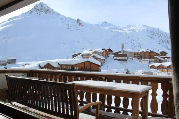 A snow-covered mountain with a ski lift in the background and wooden buildings with snow on their roofs.