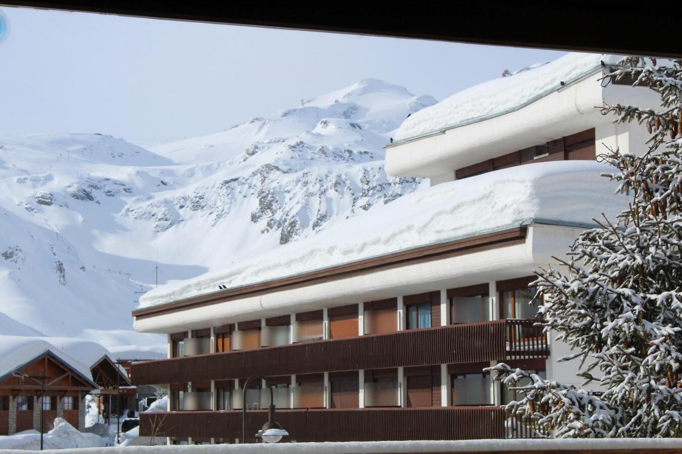 A hotel with a modern design, featuring a multi-story structure with balconies. The building is surrounded by snow-covered mountains, indicating a winter setting.