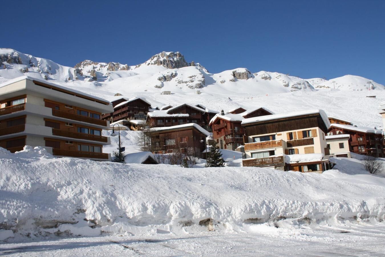Una località turistica montana innevata, con edifici a più piani, piste da sci e un cielo azzurro limpido.