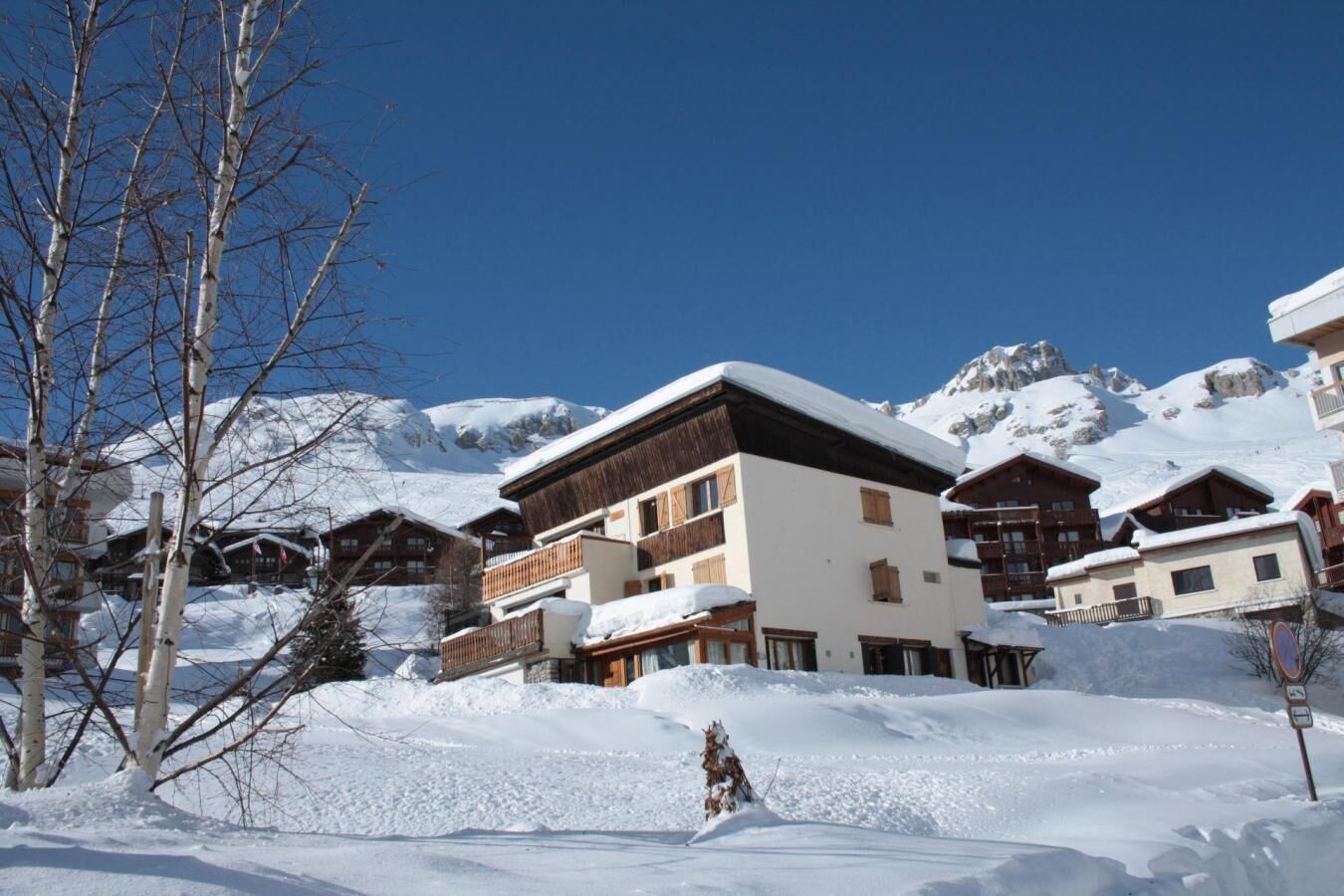 Une station de montagne enneigée, avec des bâtiments de style chalet, un ciel dégagé et une piste de ski au premier plan.