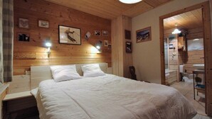 Una habitación acogedora de madera con una cama grande, una mesita pequeña y un baño a la vista, visible a través de una puerta abierta.