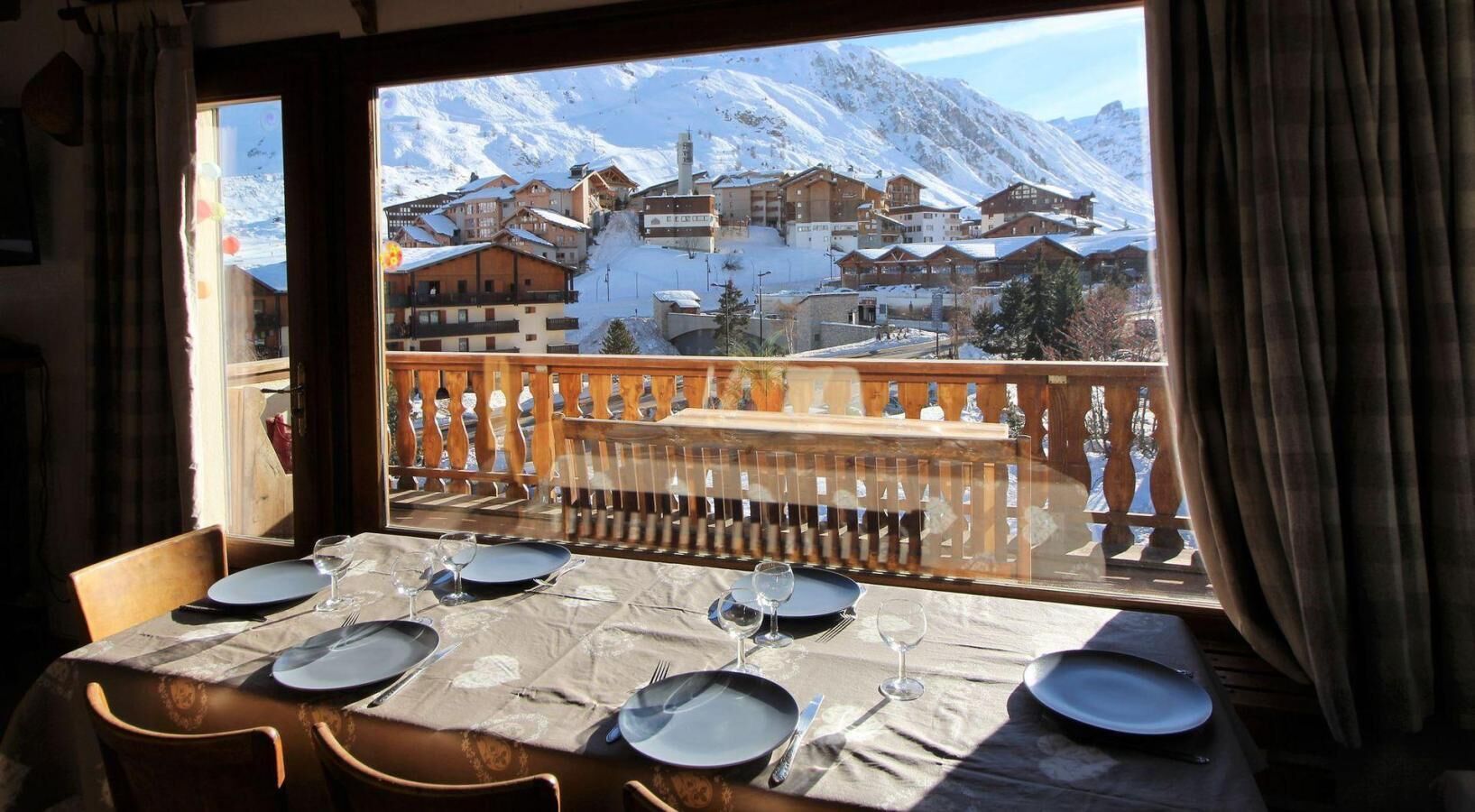 A dining table set for six with a view of a snowy mountain village.