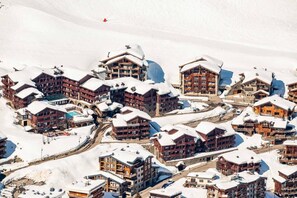 A snow-covered mountain resort with multiple chalet-style buildings, ski lifts, and a clear view of the surrounding snowy landscape.