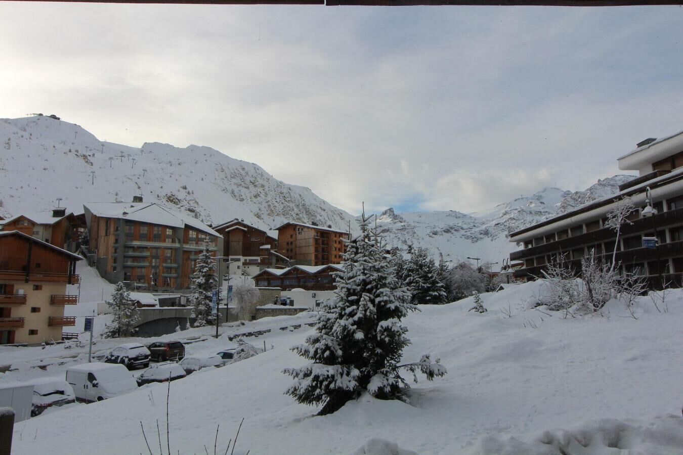 Un complejo turístico de montaña cubierto de nieve con edificios de madera, un telesilla y un árbol nevado.