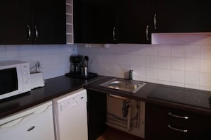 A compact kitchen with dark cabinets, a microwave, a toaster, a sink, and a dishwasher.
