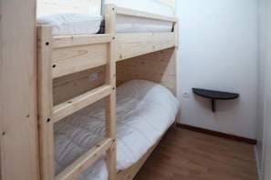 A bunk bed with a shelf attached to the wall, a wooden floor, and a white wall.