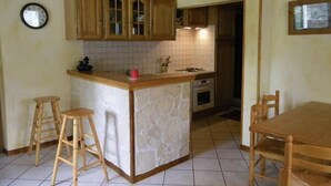 A kitchen with wooden cabinets, a central island with stools, a clock on the wall, and a window.