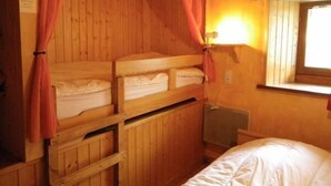 A cabin-style room with bunk beds, a window with curtains, and a wall-mounted light fixture.