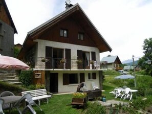 Un chalet de dos pisos con balcón, mobiliario exterior y jardín.