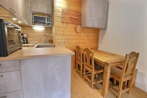 A compact kitchen with a microwave, oven, and sink. There is a wooden dining table with chairs. - 150m from ski slopes, 1st floor, balcony, 38m², Méribel-Mottaret (Méribel - Les Allues)