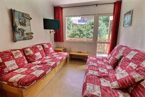 A cozy room with two red and white patterned sofas, a flat-screen TV, and a window with red curtains. - 150m from ski slopes, 1st floor, balcony, 38m², Méribel-Mottaret (Méribel - Les Allues)