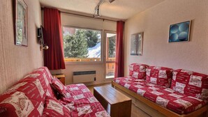 A cozy room with two red upholstered sofas, a wooden coffee table, and a large window with red curtains. - 150m from ski slopes, 1st floor, balcony, 38m², Méribel-Mottaret (Méribel - Les Allues)