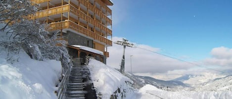 A multi-story building with balconies, a staircase leading up to it, and a snowy landscape in the background.