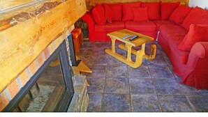 A cozy room with a red sofa, a wooden table, and a fireplace. - Chalet, balcony, fireplace or stove, parking, tv, ski locker, 260m², Les Menuires (Saint-Martin-de-Belleville)
