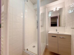 Ein modernes Badezimmer mit einer Duschkabine aus Glas, einem Waschbecken mit Spiegel darüber und Holzschränken.