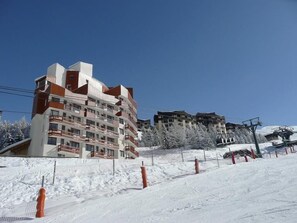 Ein mehrstöckiges Hotel mit Balkonen, gelegen in einer verschneiten Gegend mit Skipisten im Hintergrund.