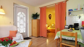 A cozy room with a bed, a dining table, a kitchen area, and a door leading to another room. - Apartment 2 - Us Klausing (Heringsdorf)