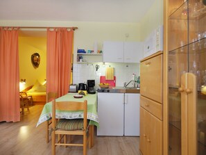 A compact kitchen with a dining table, chairs, a coffee maker, and a cabinet.