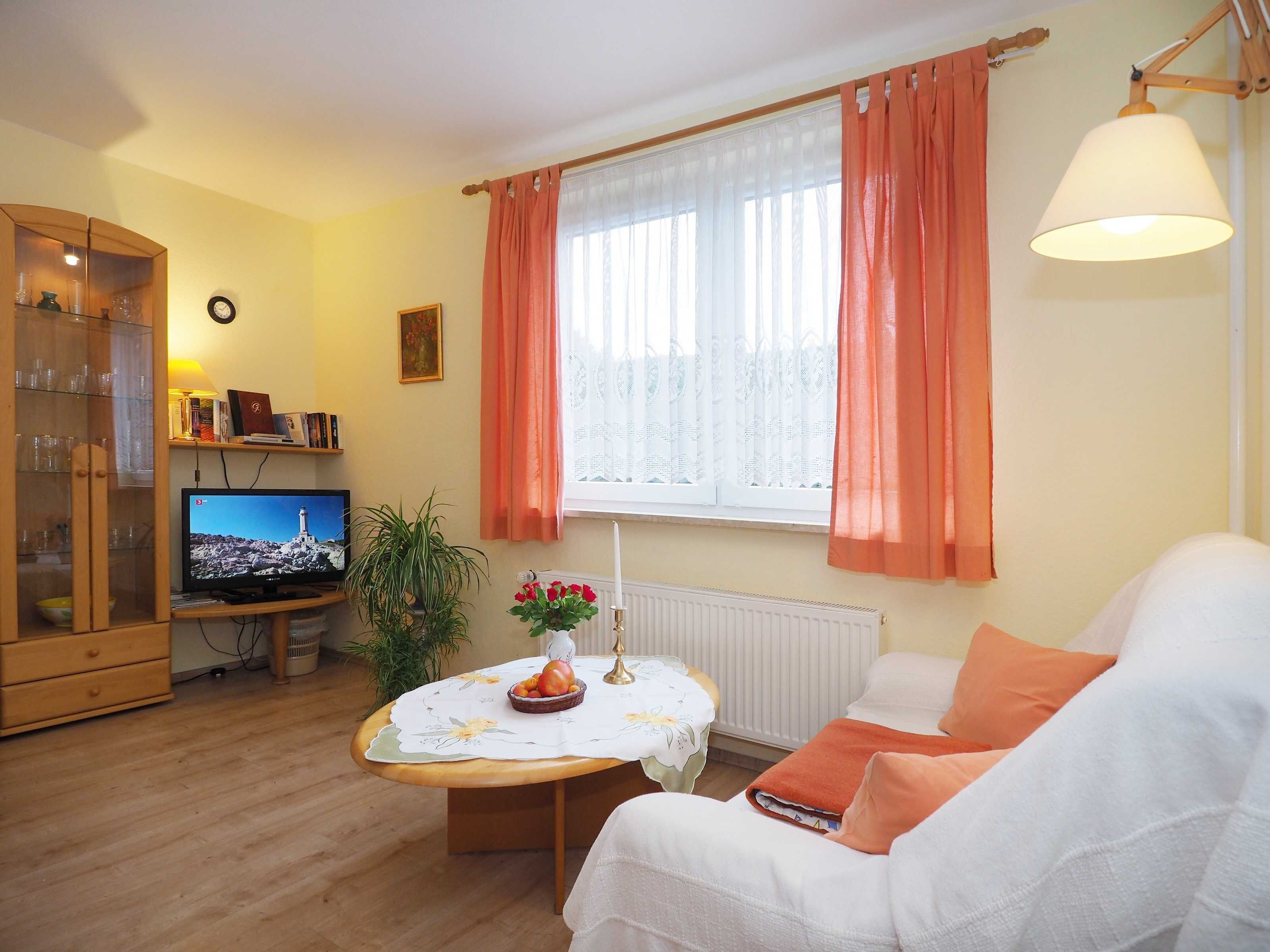 A living room with a television, a dining table with a flower vase, a sofa, and a cabinet.