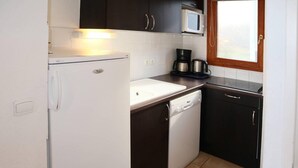 A compact kitchen with a white refrigerator, a coffee maker, a dishwasher, and dark cabinets. - 200m from shops, swimming pool, sauna, hammam, terrace, balcony, ski locker, 43m², Les Orres (Les Orres)