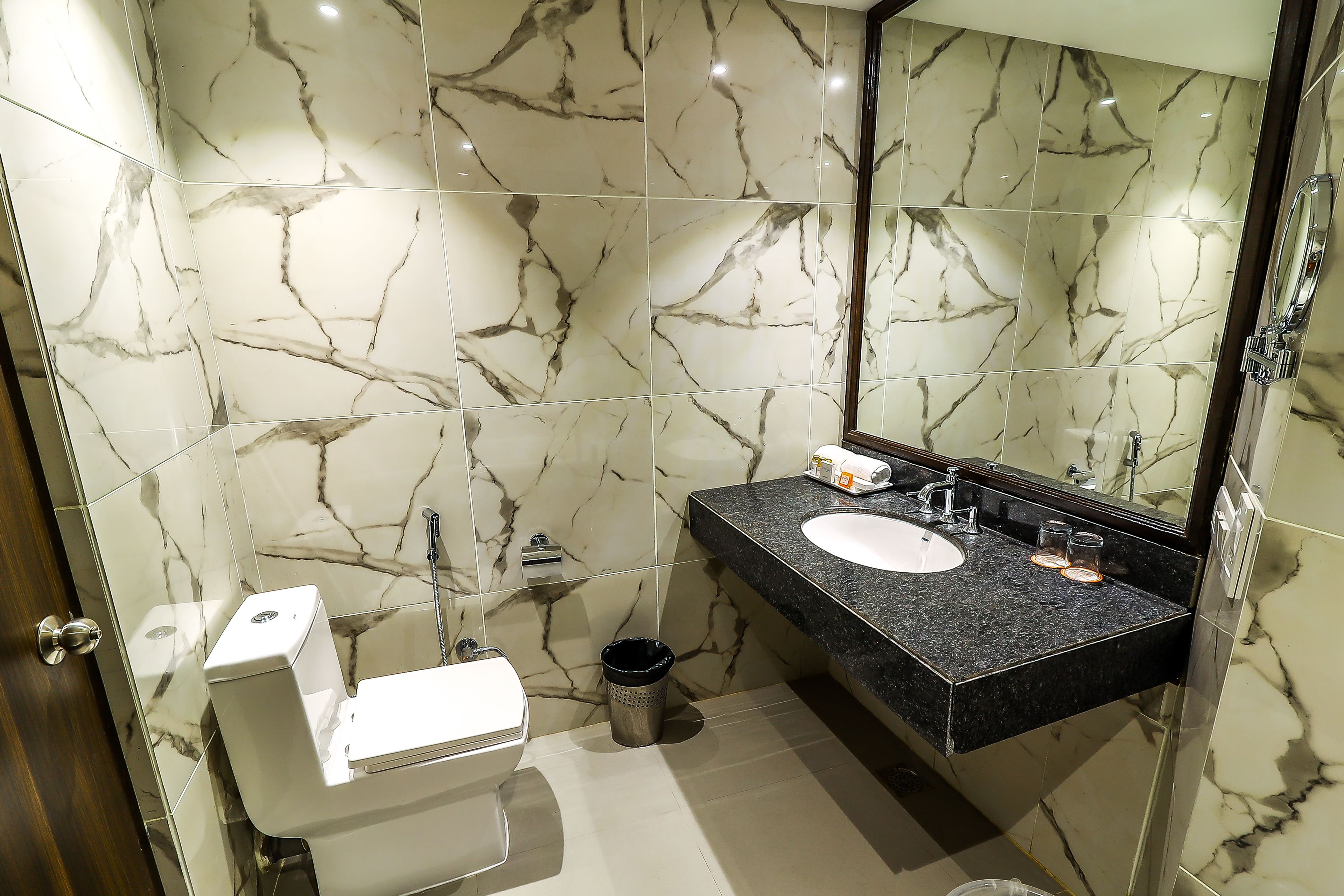 A bathroom with marble walls, a white toilet, a black sink, and a mirror.