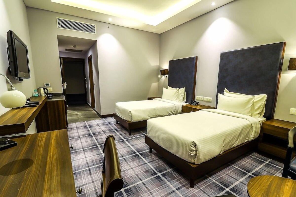 Ein Hotelzimmer mit zwei Betten, einem Schreibtisch, einem Sessel, einem Fernseher und einer Badezimmertür.