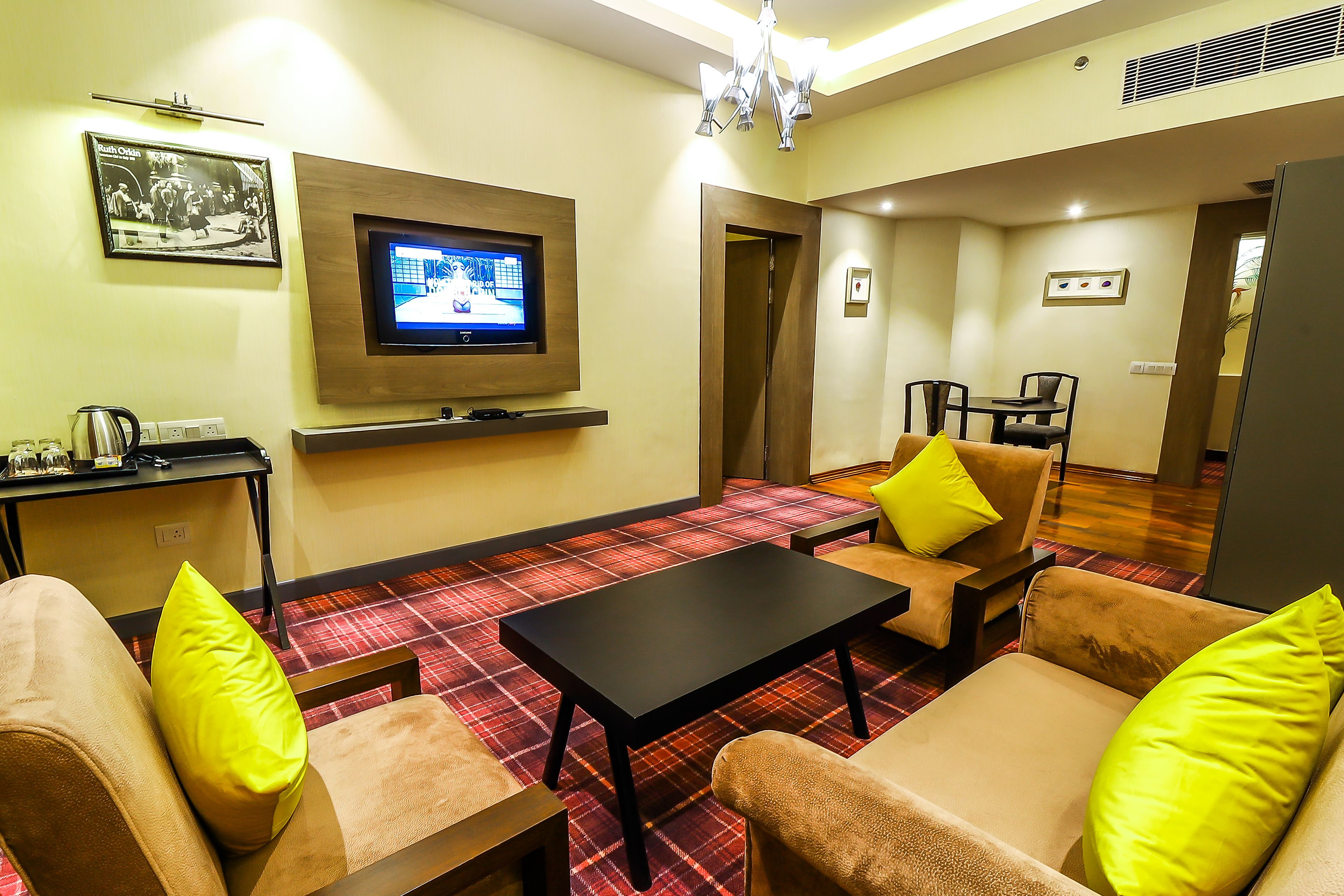 A living room with a flat-screen TV, a coffee table, and two sofas with yellow pillows.
