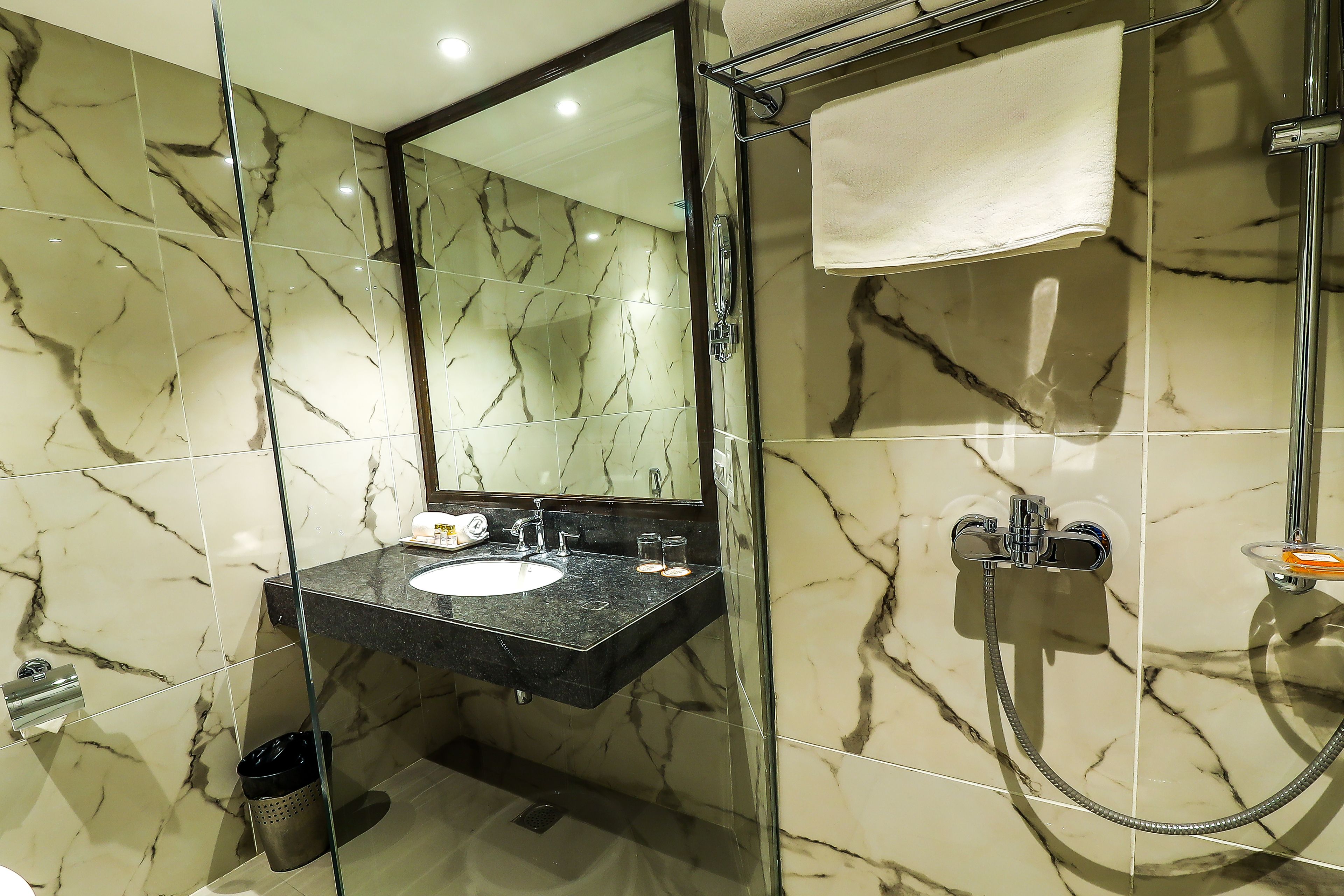 A bathroom with a marble-tiled wall, a glass-enclosed shower, and a sink with a mirror above it.