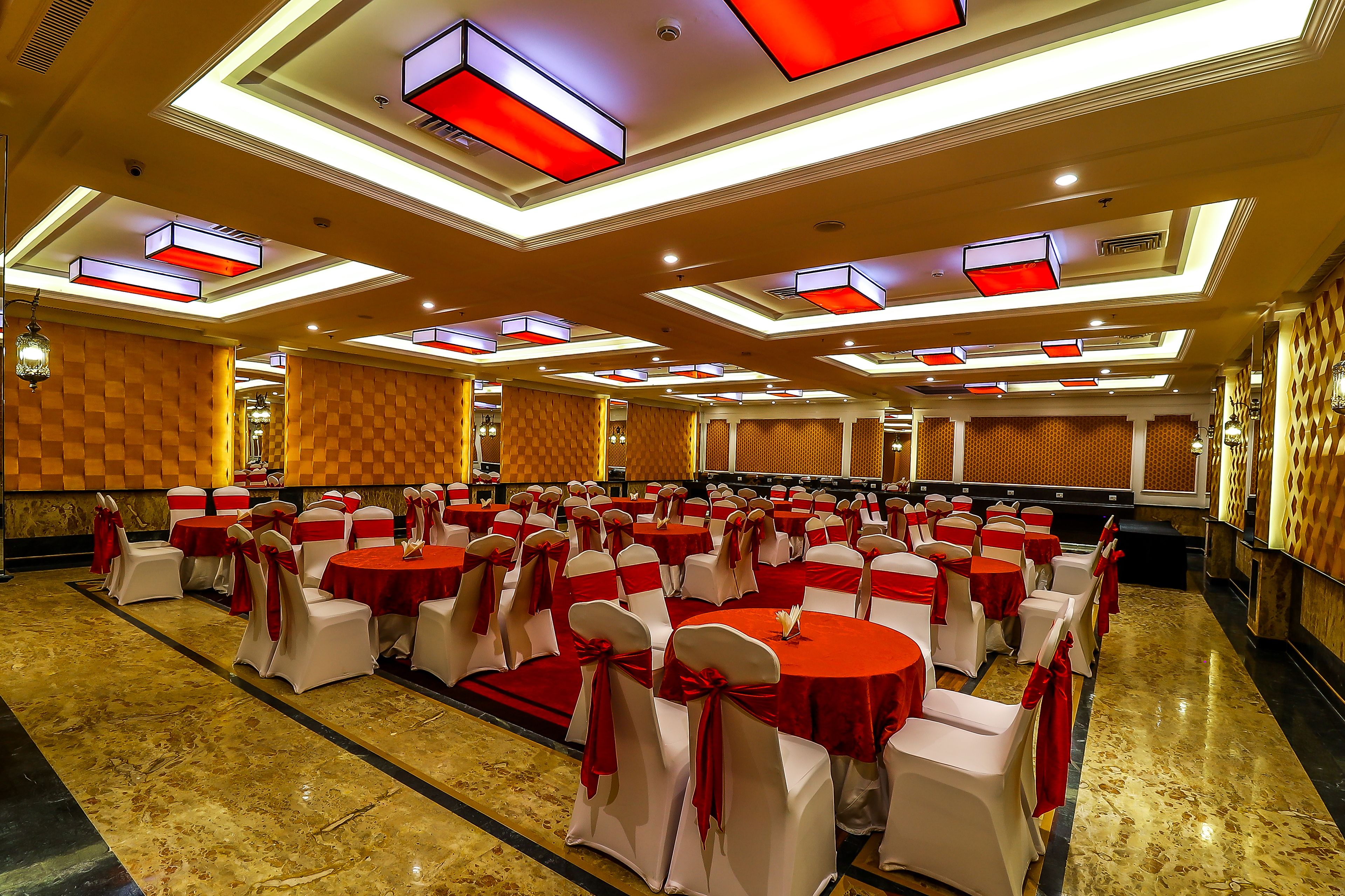 A banquet hall with rows of round tables, each with a red tablecloth and white chairs, set up for a formal event.