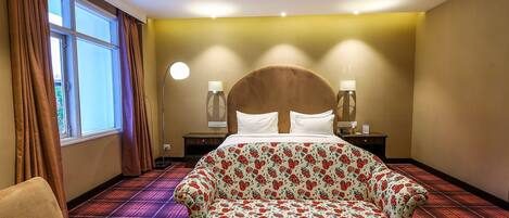 A hotel room with a large bed, a sofa, a chair, and a nightstand with lamps.