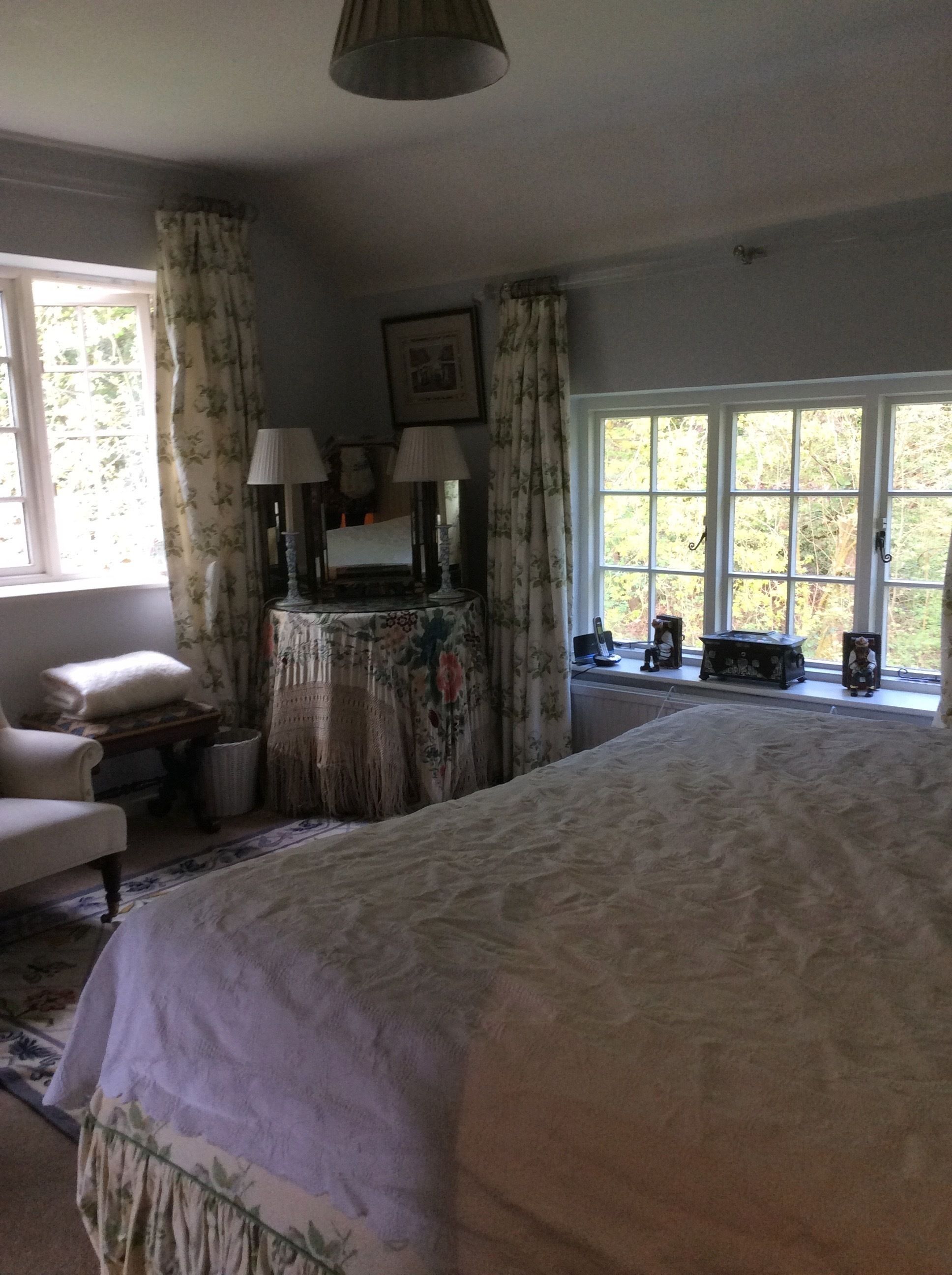 A bedroom with a large bed, a chair, a vanity with a mirror, and a window with curtains.