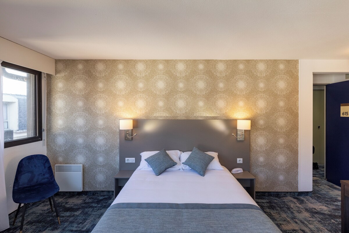 A hotel room with a large bed, two bedside lamps, a chair, and a patterned wall.