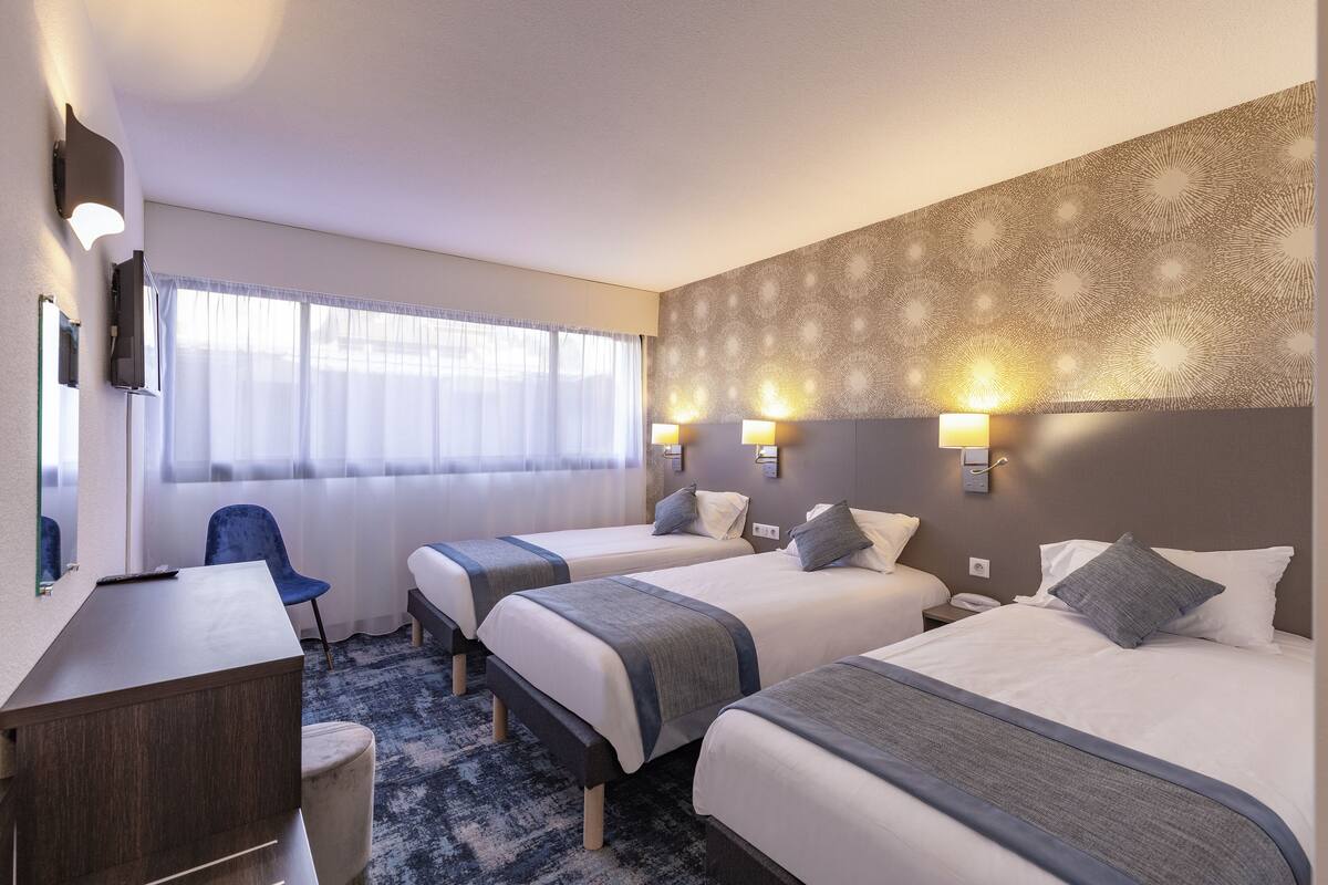 Habitación de hotel con tres camas, un escritorio, una silla y un papel tapiz estampado.