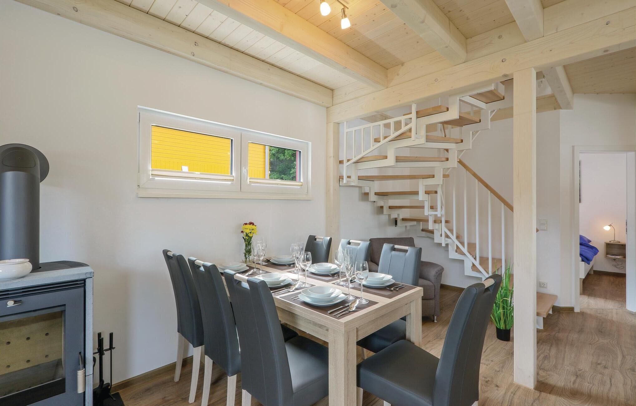A dining area with a wooden table set for six, a modern stove, and a staircase with a white railing.