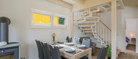 A dining area with a wooden table set for six, a modern stove, and a staircase with a white railing.