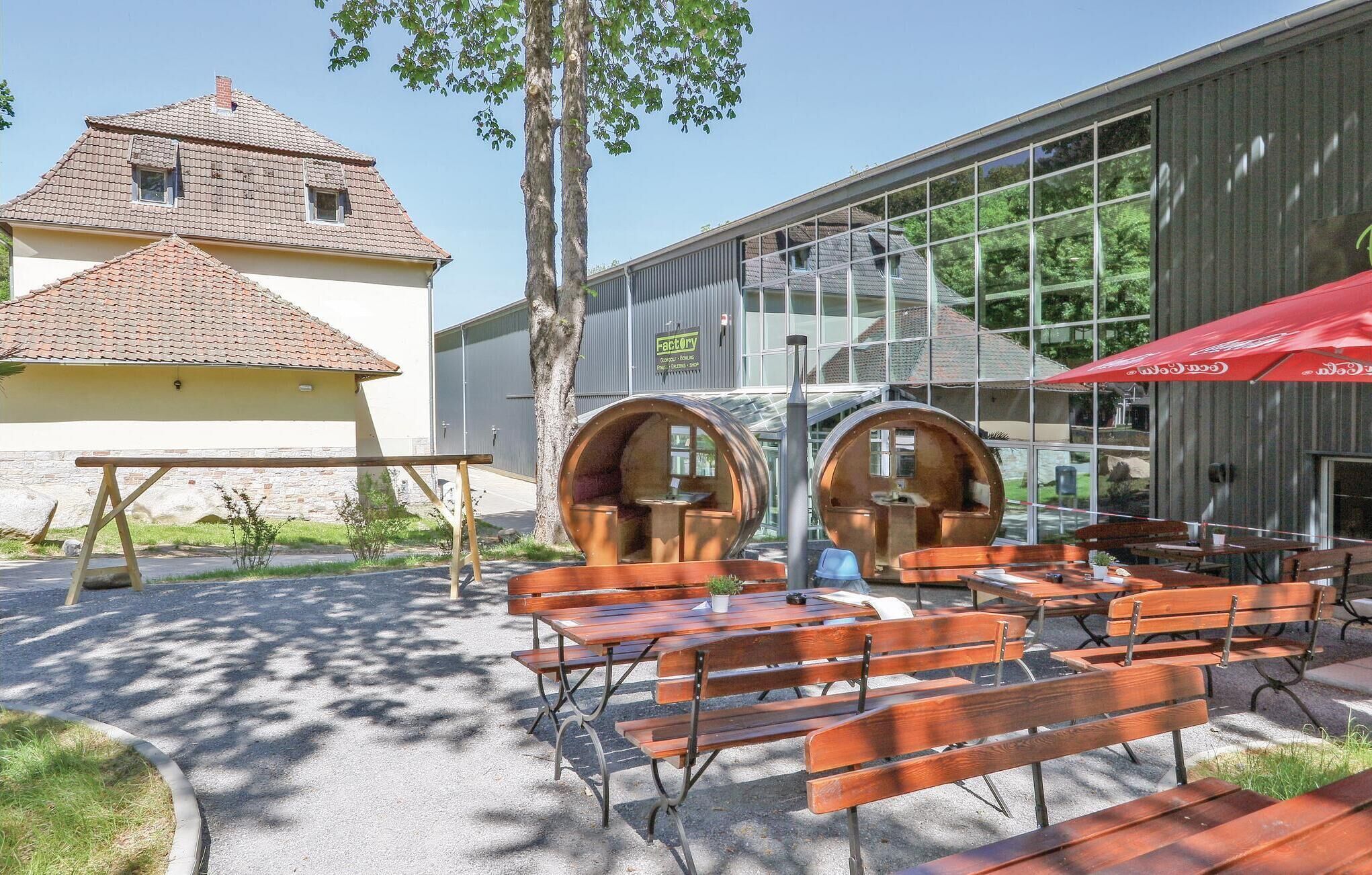 An outdoor seating area with wooden benches and tables, a red umbrella, and a building with large windows and a sign that reads "Factory."