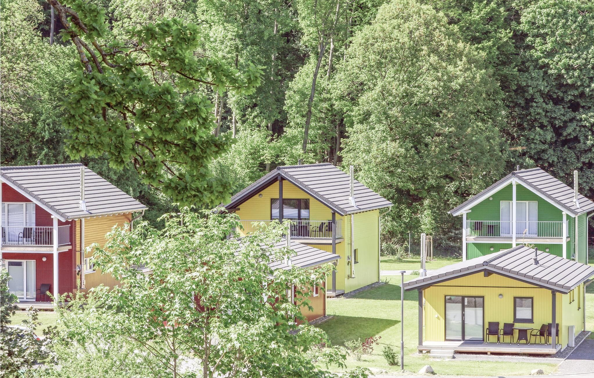 Tres cabanes petites i colorades amb teulades inclinades, envoltades per arbres densos.