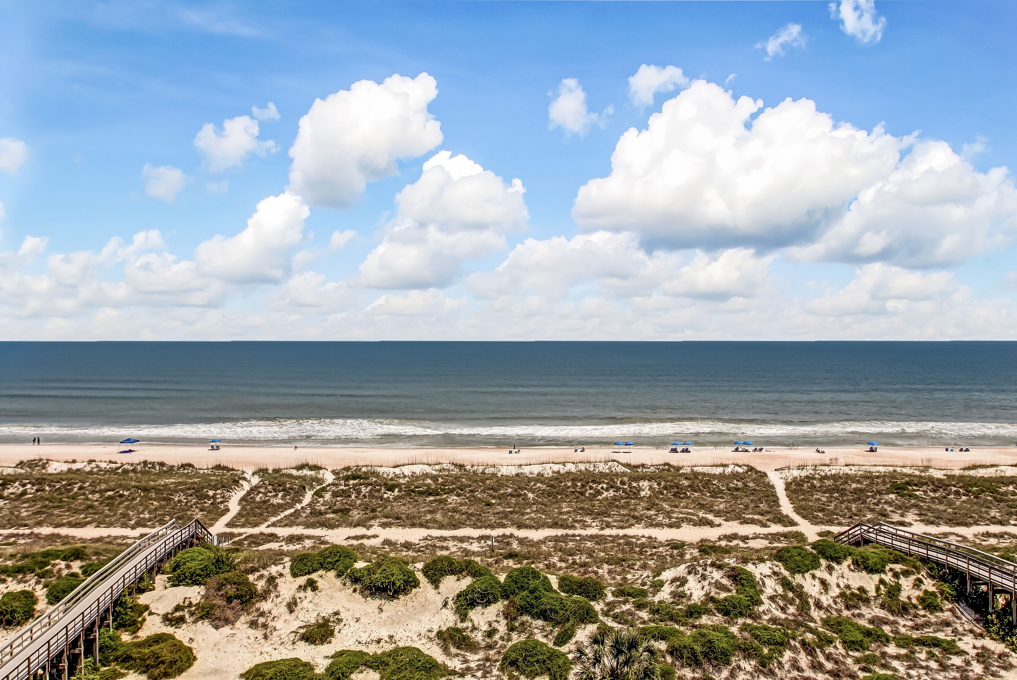 Ein Strand mit einer Holzpromenade, Sanddünen und freiem Blick auf den Ozean.