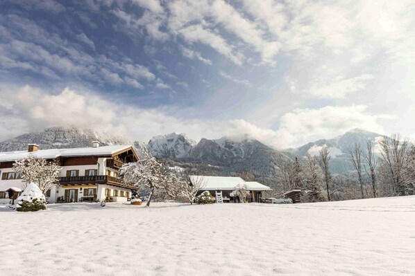 Un bâtiment enneigé doté d’un balcon, entouré d’arbres couverts de neige et avec des montagnes enneigées en arrière-plan.