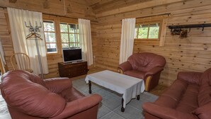 A cozy cabin interior with a wooden interior, leather sofas, a television on a wooden stand, and a window with curtains. - Kotkanpesä by Interhome (Masku)